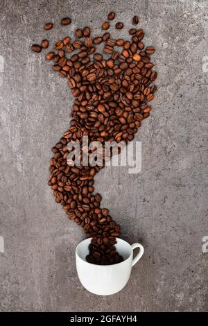 Verschüttete Tasse Kaffee mit gerösteten Bohnen, die eine Rauchform bilden, vertikal Stockfoto