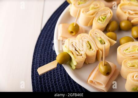 Partysnacks. Crepe Rolls mit Schinken und Käse auf einem mit Oliven verzierten Stock Stockfoto