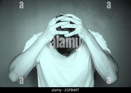 Graustufenaufnahme eines Mannes, der seinen Kopf mit den Händen hält, sich verstört und gestresst fühlt Stockfoto