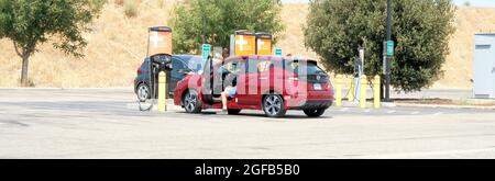 Mann sitzt in seinem Auto und lädt ein Nissan Leaf Elektrofahrzeug an einer ChargePoint Express DC Schnellladestation, die sich an einer Autobahn in der Nähe von Gilroy, Kalifornien, befindet. Stockfoto