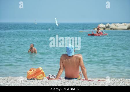 Sitzender Mann genießt die Sonne am Kiesstrand Stockfoto