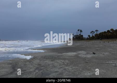 Entferntes Paar, das an der Küste eines Sandstrandes in einem Sturm, starker Brandung und dunklen Wolken, horizontaler Aspekt läuft Stockfoto