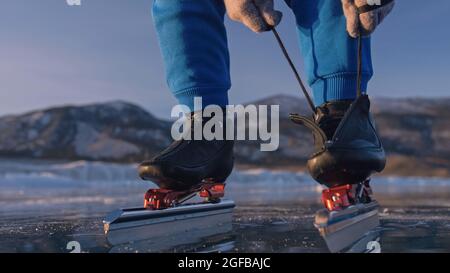 Das Kind trainiert auf Eisschnelllauf. Sportler zieht Schlittschuhe an. Das Mädchen Schlittschuhe im Winter in Sportkleidung, Sportbrille. Zeitlupe im Freien. Stockfoto