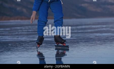 Das Kind trainiert auf Eisschnelllauf. Das Mädchen Schlittschuhe im Winter in Sportbekleidung, Sportbrille, Anzug. Zeitlupe im Freien. Stockfoto