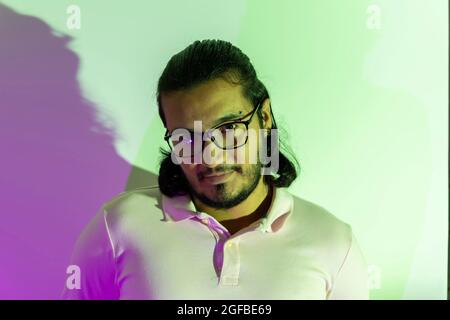 Junger Latino-Mann, der mit farbigen Lichtern auf die Kamera schaut Stockfoto