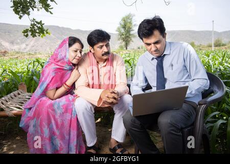 Glückliche ländliche indische Bauernfamilie mit Agronom oder Bankier verwenden Laptop. Ein Beamter, der die Richtlinie auf dem Computerbildschirm, der finanziellen Unterstützung oder der cro für die Landwirtschaft zeigt Stockfoto