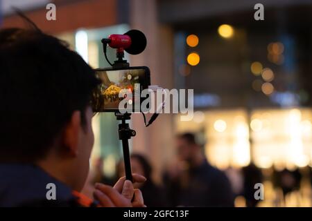 Content Creator, der durch den Weihnachtsmarkt von Manchester geht und ein mit dem Pixel 4 aufzeichnendes Video mit dem Mikrofon von Salto für vlog aufzeichnet. Stockfoto