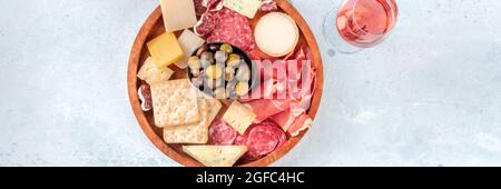 Panorama von Aufschnitt und Käseplatte, von oben mit Rosenwein aufgenommen. Aufschnitt, Blauschimmelkäse, Oliven. Feinkost mit einem Getränk Stockfoto