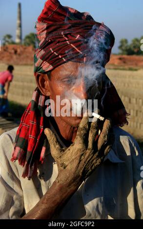 Porträt eines Mannes, der in einer Ziegelfabrik eine Zigarette raucht. Bangladesch. Stockfoto