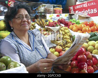 Cajamarca, Peru. Die von Obst umgebene Kauffrau aus Peru liest in ihrem Obststall auf dem Stadtmarkt ein Nachrichtenblatt. März 2010 Stockfoto