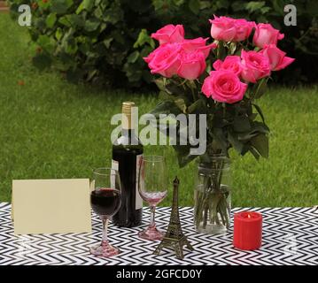 Rosenstrauß auf dem Tisch im Freien mit Wein und Kerze Stockfoto