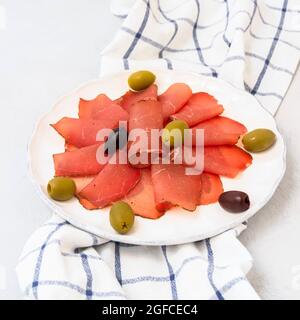 Köstliche Pastrami-Scheiben aus gebratenem Rindfleisch auf weißem Tisch mit Oliven Stockfoto