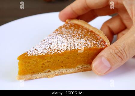 Die Hand des Mannes pflückt ein Stück leckerer Kürbiskuchen von White Plate Stockfoto