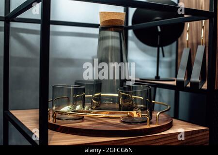 Tablett mit elegantem dunklen Glasdekanter und Gläsern auf dem Regal. Leere transparente Karaffe mit Holzkorken und Gläsern als Dekor. Stockfoto