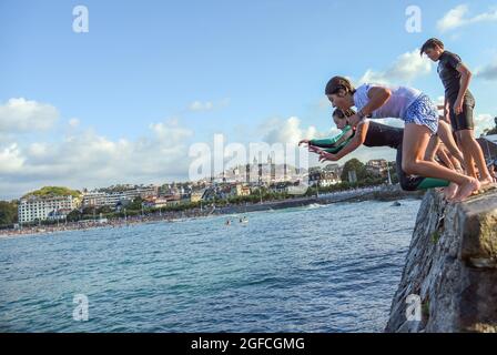 San Sebastian, Spanien. August 2021. Junge Leute tauchen in das Meerwasser und machen akrobatische Sprünge am Strand La Concha in San Sebastian.Jugendliche genießen diesen Sommer den Sprung von der Wand am Ende der Promenade von Playa de la Concha de San Sebastian neben dem Monte Igueldo mit spektakulären Sprüngen und ohne Die Gefahr, dass die Steinklippen für diese Art von Sprüngen bieten. Kredit: SOPA Images Limited/Alamy Live Nachrichten Stockfoto