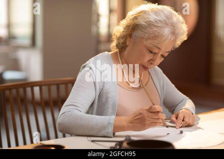 Ältere Frau übt im Arbeitszimmer Kalligraphie Stockfoto