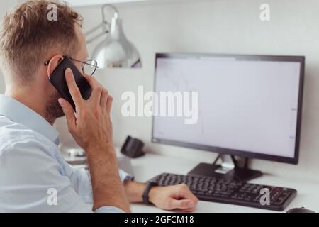 Der junge Geschäftsmann brocker am Mobiltelefon im Büro. Investitionen, Handel mit Aktien an der Baisse. Stockfoto