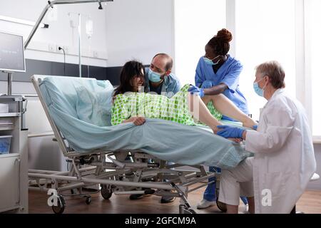 Multiethnisches medizinisches Team, das bei der Entbindung von Kindern auf der Krankenhausstation hilft. Frau gebiert Baby, während sie im Bett mit Wehen Kontraktionen lag. Arzt und schwarze Krankenschwester bei der Geburt Stockfoto