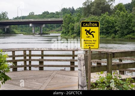 Vorsicht Gehweg im Winter nicht gepflegt Schild, das zur Aussichtsplattform am Fluss führt. Bild einer Person, die rutscht und fällt. Stockfoto