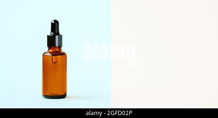 Ein Nachbau einer leeren Glastropfflasche aus braunem Bernsteinglas auf blauem Hintergrund. Hautpflegeserum, Banner oder Schablone. Das Konzept eines Naturkosmetikprodukts.Copyspace. Stockfoto