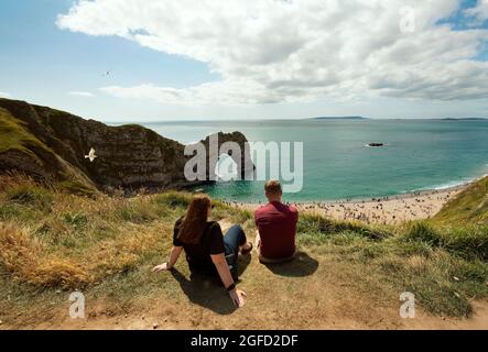 Durdle Door, die ikonischste Landschaft der Jurassic Coast mit ihrem natürlichen Kalksteinbogen. Junges Paar genießt einen sonnigen Sonntag. Dorset, Großbritannien. 22 August 2021 Stockfoto