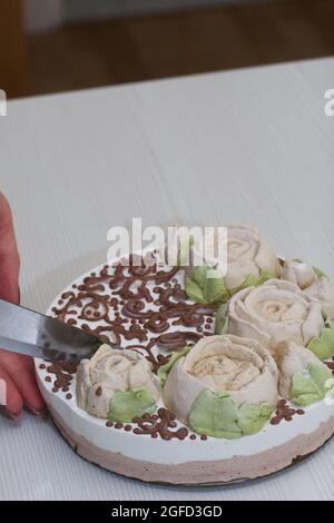 Eine Frau schneidet den Milchkuchen eines Vogels, der mit marmelallow-Rosen und Schokolade geschmückt ist. Stockfoto