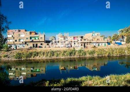 Palmen und Wohngebäude in der Nähe des Bewässerungskanals im Niltal. Ägypten. Stockfoto