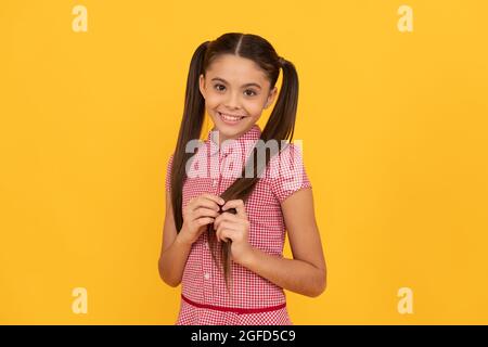 Glauben Sie an Schönheit. Schüchternes Mädchen gelber Hintergrund. Kind mit schüchternem Lächeln berühren die Haare Stockfoto