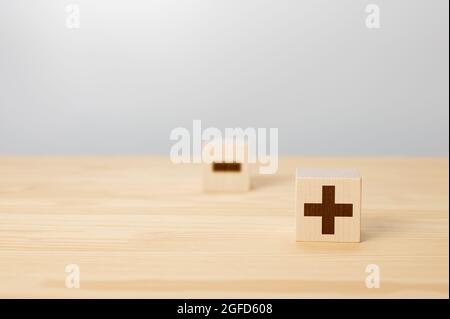 Vor- und Nachteile Konzept. Wahl von Plus mit verschwommenem Minus-Symbol. Konzept der Gegensätze, Holzblock mit Plus und Minus auf grauem Hintergrund, Holzwürfel Stockfoto