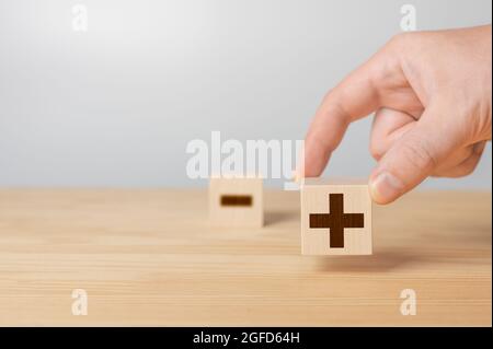 Holzwürfel mit dem Bild von vor- und Nachteile. Plus oder Minus. Geschäftsmann hält einen Würfel mit Plus-Symbol. Holzwürfel mit Minus-Symbol. Holzwürfel wi Stockfoto