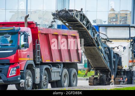 Die Kaltfräsmaschine der Straße entfernt den alten Asphalt und die Beladung in einen Muldenkipper. Reparatur des Asphaltbelags der Straße Stockfoto