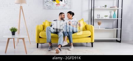 Junges multiethnisches Paar mit Gadgets auf Couch, Banner Stockfoto