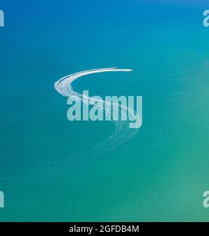 Wassersport am Strand. Schnellboot und Wellengleiter verlassen Zickzackpfad auf dem Wasser, Blick von oben Stockfoto