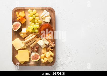 Käseplatte mit Trauben, Nüssen, Feigen und Honig in Holzplatte auf weißem Hintergrund mit Kopierfläche. Blick von oben. Festliche Gourmet-Vorspeise. Stockfoto