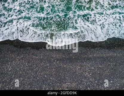Stürmisches Wetter, Meereswellen brechen an einem Ufer mit schwarzem vulkanischem Sand, Hintergrund mit Kopierraum Stockfoto