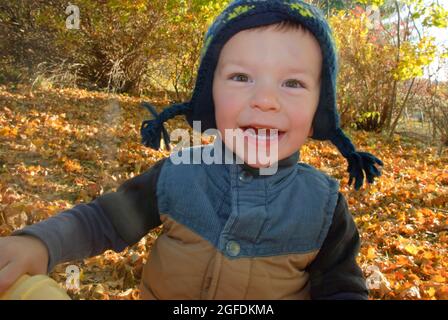 Nahaufnahme eines kleinen Jungen, der in den Herbstblättern spielt Stockfoto