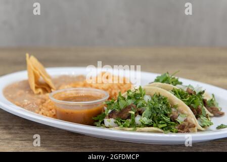 Herzhafte Platte mit drei geladenen Carne Asada Tacos mit Koriander, serviert mit Reis und gebratenen Bohnen. Stockfoto