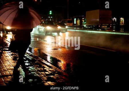 Regnerischer Abend. Eine Frau Silhouette mit Regenschirm und laufendem Verkehr mit Regentropfen. Herbstzeit. Stockfoto