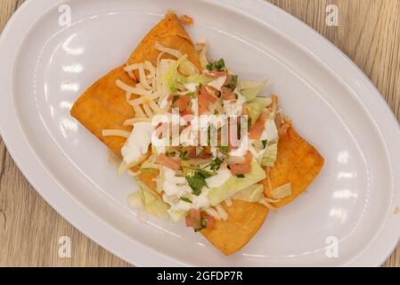 Blick von oben auf eine herzhafte Vorspeise von zwei Enchiladas, die mit saurer Creme, Pico de gallo und Käse bedeckt sind. Stockfoto