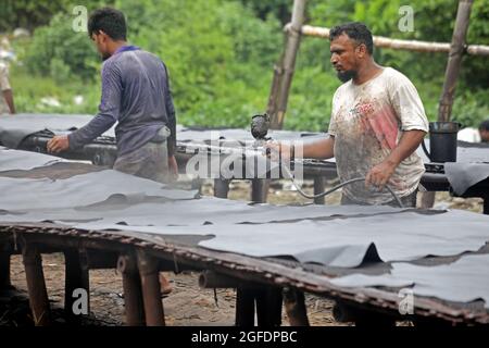 Dhaka, Bangladesch, 25. August 2021: Arbeiter von Hazaribagh malen Leder als Teil des Fertigungsprozesses der Ledergerbung in einer kleinen Fabrik, um es zur Herstellung von Schuhen zu verkaufen. Beim Bräunen werden die Häute eingeweicht, um das Salz in einer Lösung aus Kalk und Wasser zu entfernen, um das Haar zu erweichen und mit einer Maschine zu beseitigen, dann werden die Rückstände von Hand mit einem stumpfen Messer entfernt. Quelle: Maruf Rahman / Eyepix Group/Alamy Live News Stockfoto