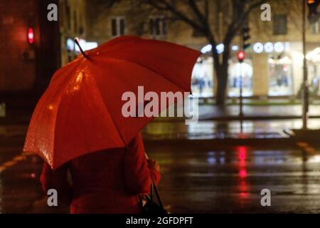 Regnerischer Abend. Eine Frau Silhouette mit Regenschirm und laufendem Verkehr mit Regentropfen. Herbstzeit. Stockfoto