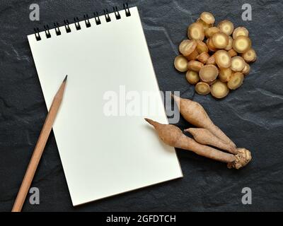 Fingerroot, Kaempfer mit offenem leerem Notizbuch und Bleistift auf schwarzem Hintergrund, Flat Lay-Konzept, Copy Space for Text. Stockfoto