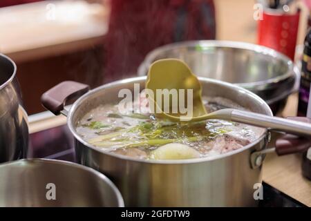 Ein Metallkochtopan, gefüllt mit kochendem Gemüse und Fleischbrühe. In der Brühe befindet sich eine Schaufel. Nahaufnahme. Stockfoto