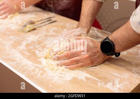 Die Hände mehrerer Personen kneten den Teig auf dem Tisch. Ein rohes Ei mit Mehl vermischen. Nahaufnahme. Stockfoto