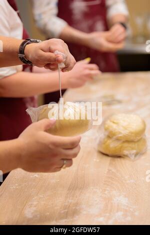 Die Hände mehrerer Personen kneten den Teig auf dem Tisch. Ein rohes Ei mit Mehl vermischen. Nahaufnahme. Stockfoto