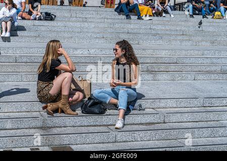 LONDON, GROSSBRITANNIEN. 25. August 2021. Zwei Frauen genießen die Sonne auf den Stufen des Trafalgar Square in London zur Mittagszeit an einem warmen und sonnigen Tag in London. Die Prognose geht von wärmeren Temperaturen mit einem Höchststand von 28 Grad Celsius über das Wochenende an den Feiertagen aus. Credit amer Ghazzal/Alamy Live News Stockfoto