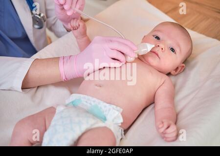 Der Arzt entfernt bei einem Neugeborenen eine laufende Nase mit einer Absaugvorrichtung. Krankenschwester in Uniform behandelt Kindernase für Grippe Stockfoto