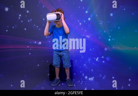 Kind sitzt und spielt mit Virtual-Reality-Brille, in einer futuristischen Umgebung. Stockfoto