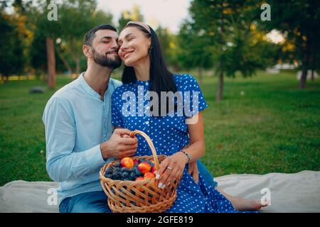 Junge Erwachsene Frau und Mann Paar sitzen mit Obstkorb auf der grünen Wiese im Park. Sommerpicknick über die Natur. Stockfoto