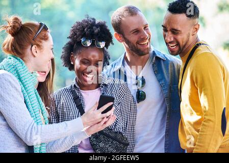 Glückliche junge Freunde mit Smartphone im öffentlichen Park Stockfoto
